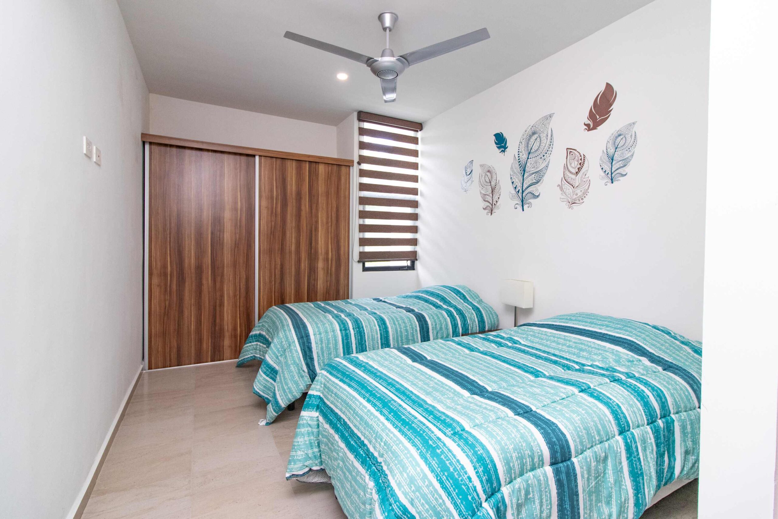 Modern bedroom with two beds covered in teal linens and feather art on the wall.