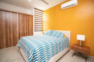 Modern bedroom with a striped blue bed cover, mustard walls, and wooden wardrobe.